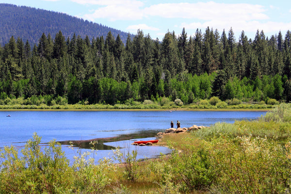Fisherman at the Edge of a lake below mountains.
